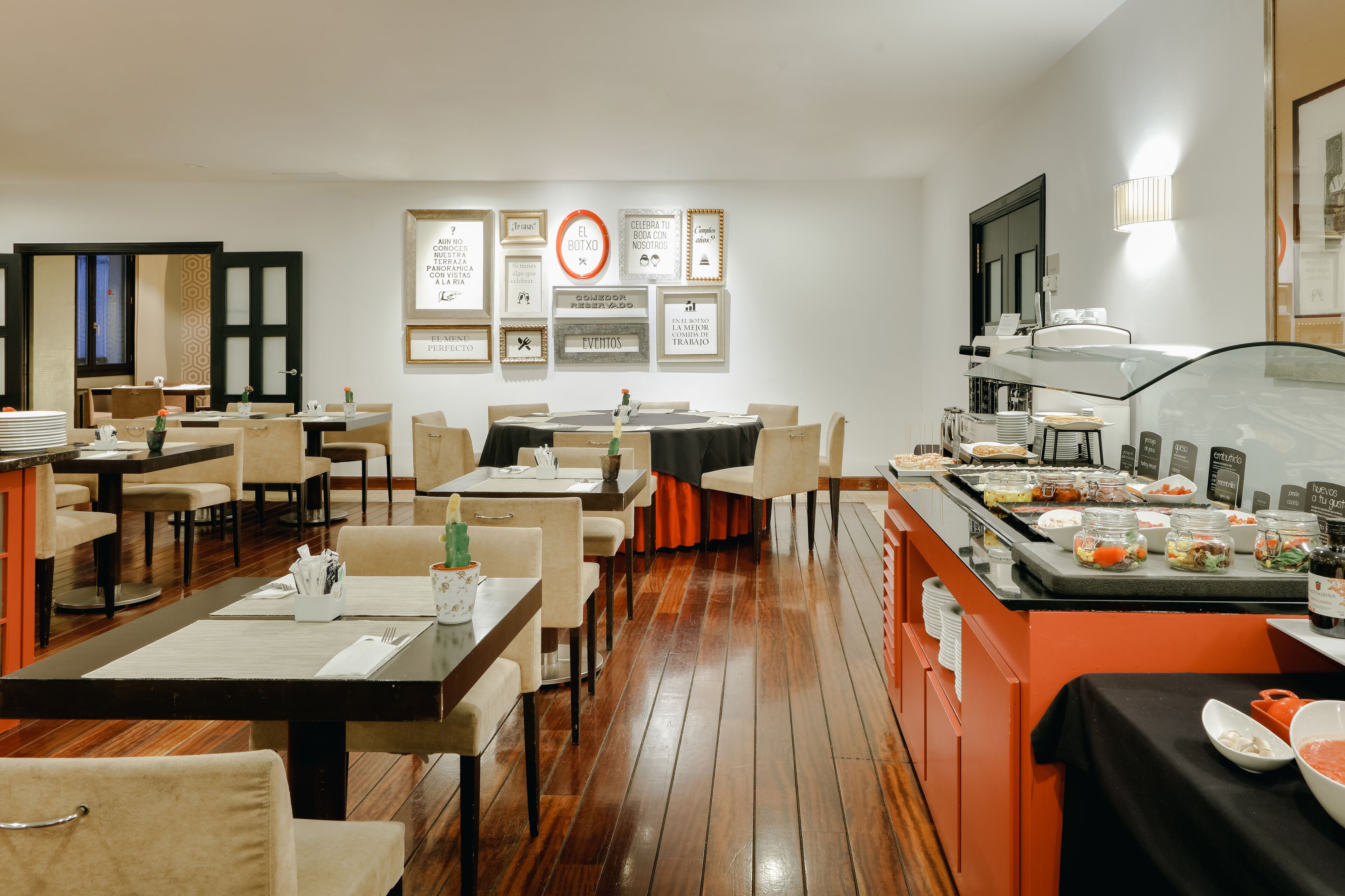 Un restaurante con varias mesas y sillas, una zona de bufé con diferentes alimentos, y citas motivacionales enmarcadas en la pared.