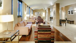A spacious hotel lobby with a long reception desk, a sofa, striped armchairs, and a coffee table. - Abba Euskalduna Hotel (Bilbao)