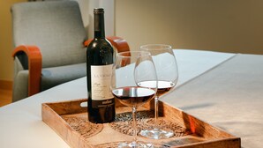 A bottle of wine and two glasses on a wooden tray on a table, with a chair and a window in the background. - Abba Euskalduna Hotel (Bilbao)