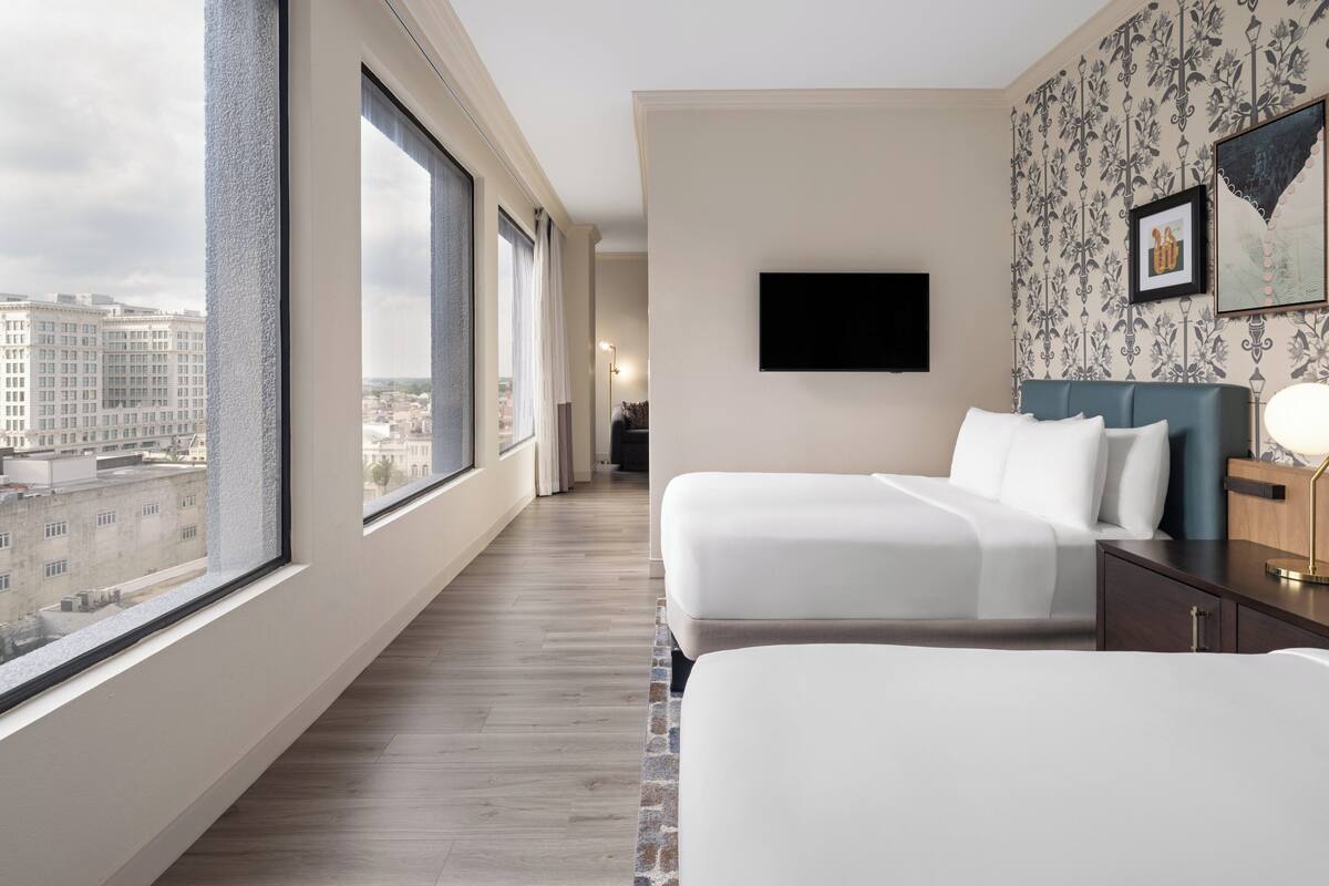 Habitación de hotel con dos camas, un televisor en la pared y un ventanal con vista a la ciudad.