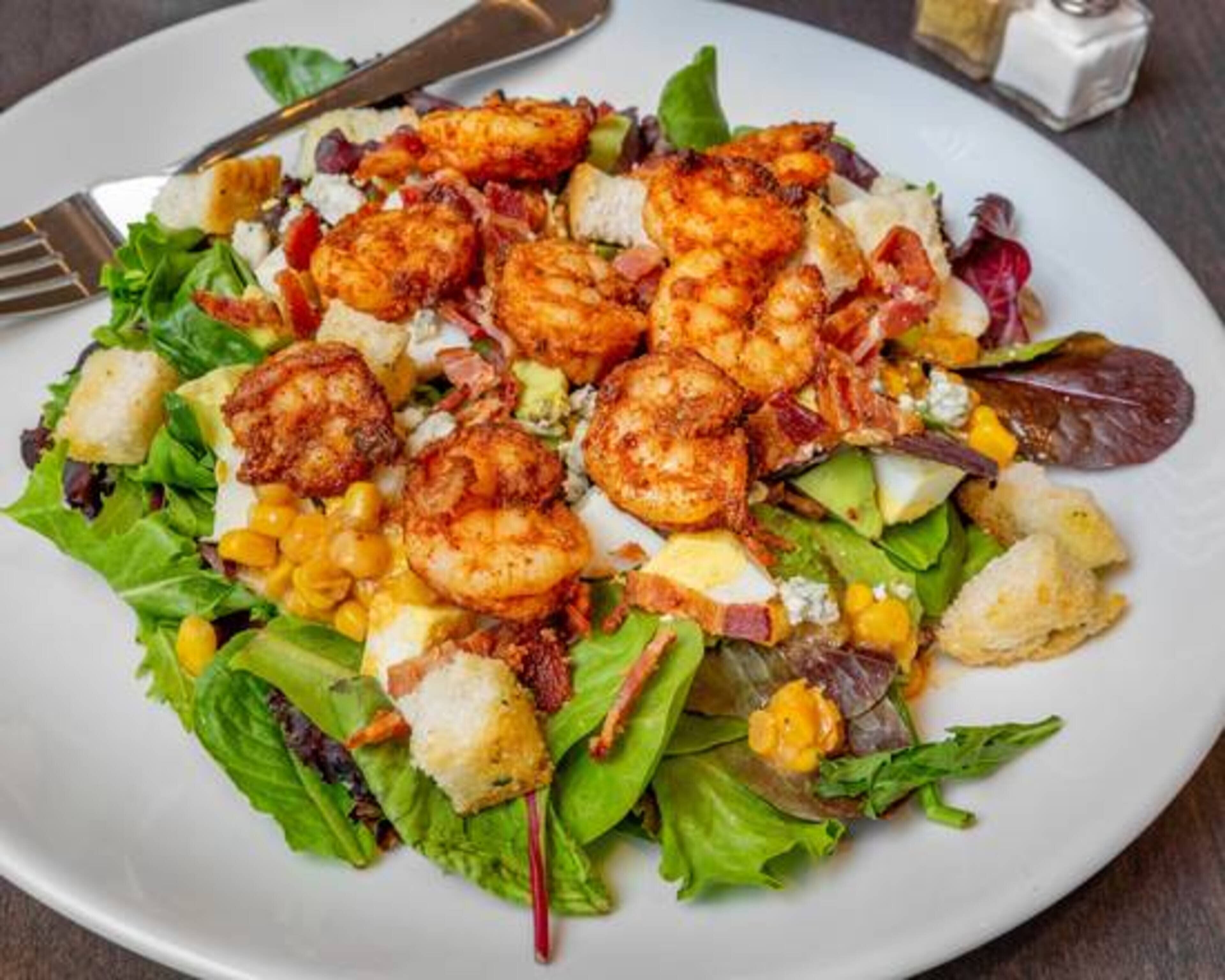 A plate of shrimp salad with lettuce, corn, and croutons.