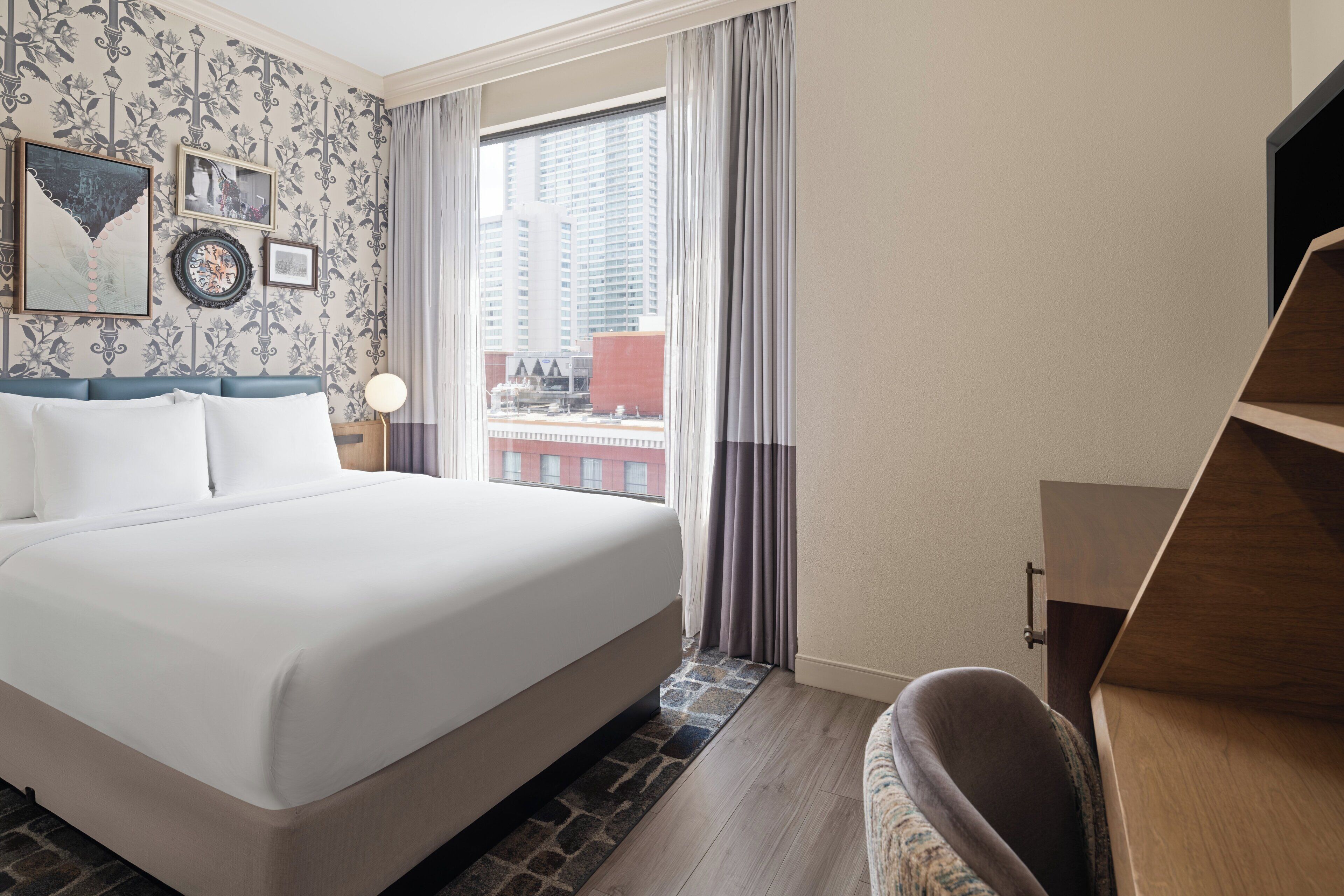 A hotel room with a large bed, a desk, and a view of the city through a window.