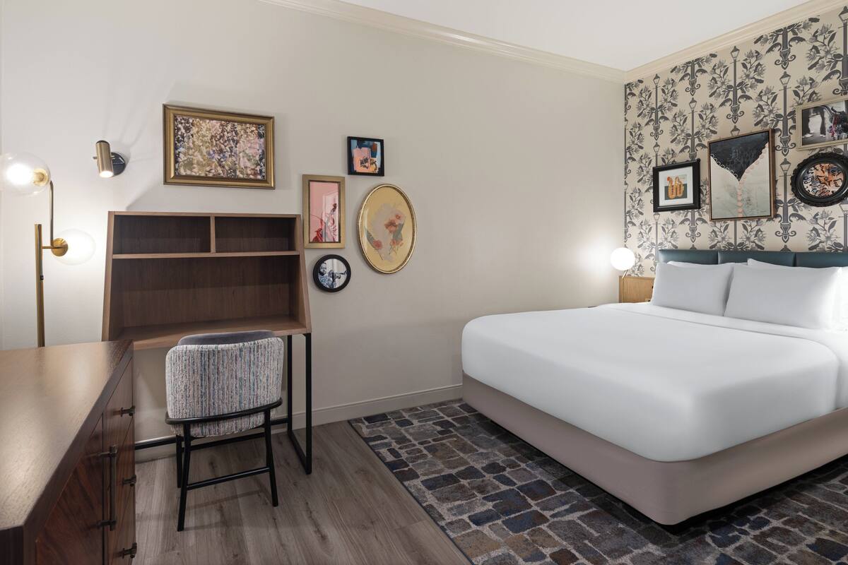 Un dormitorio moderno con cama, escritorio y silla. Hay estanterías en la pared y cuadros enmarcados.
