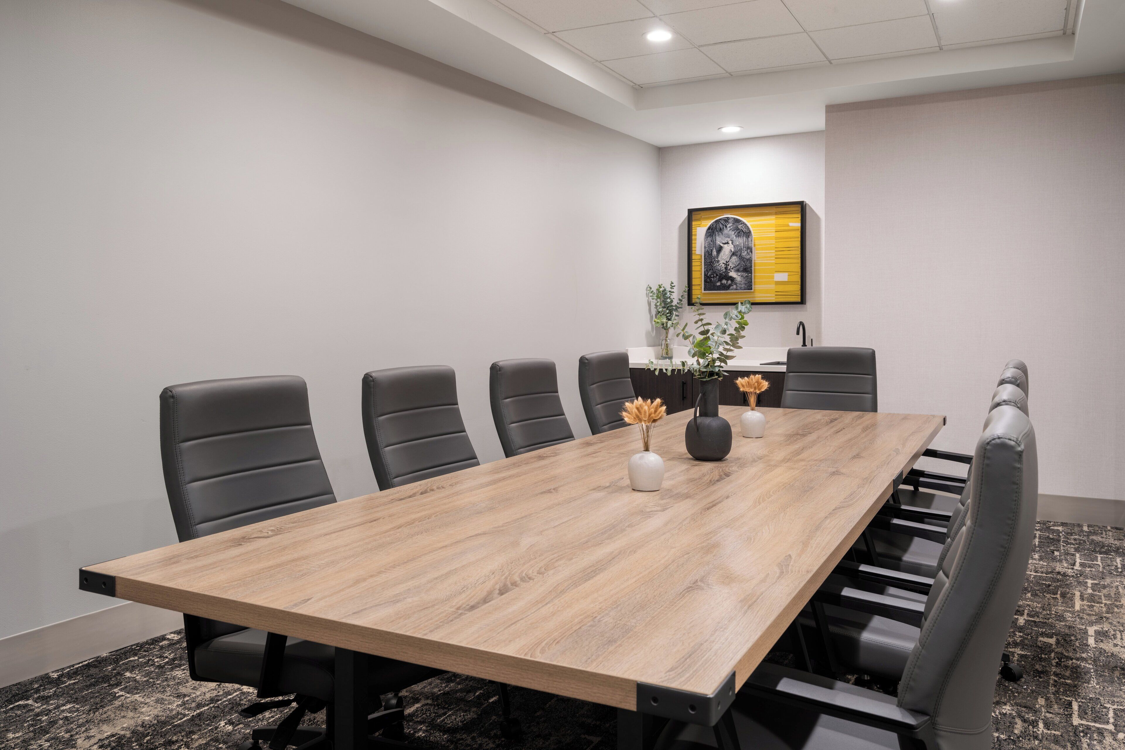 Une salle de conférence avec une longue table en bois, six chaises noires et un tableau accroché au mur.