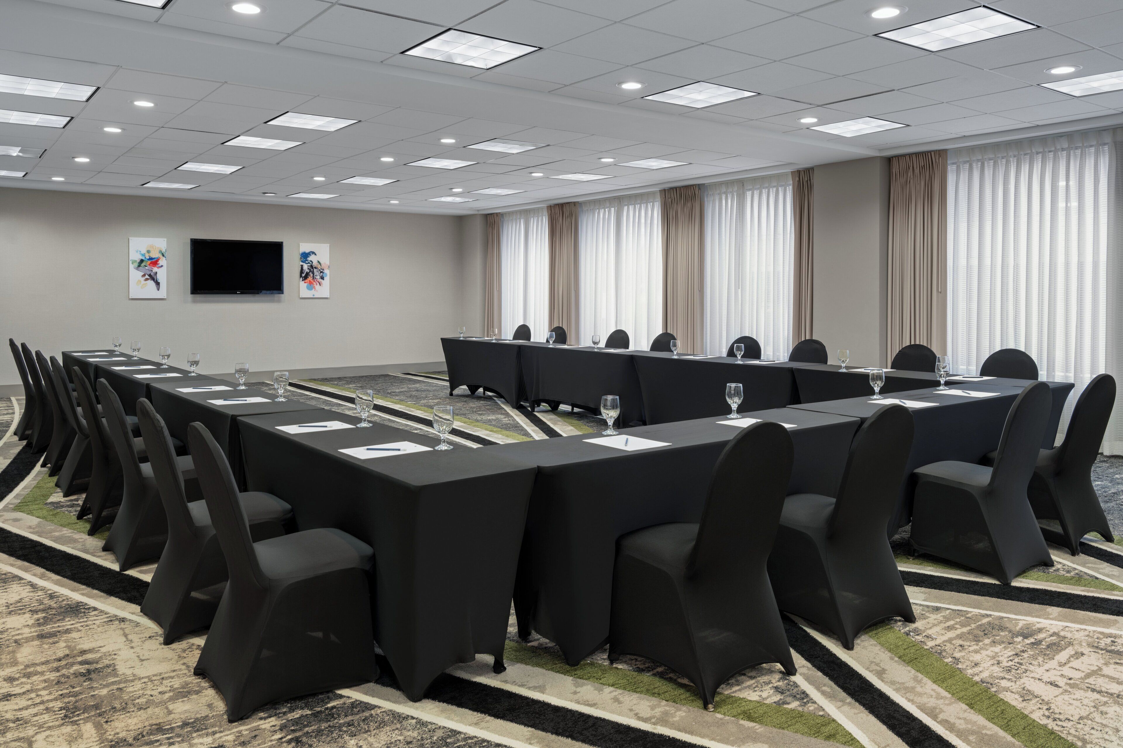 A conference room with a long table, black chairs, and a flat-screen TV on the wall.