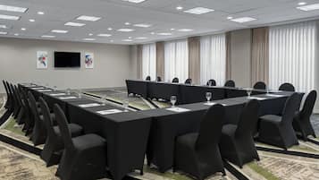 A conference room with a long table, black chairs, and a flat-screen TV on the wall.