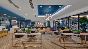 Hall d'hotel moderna con una palette di colori blu e bianco, caratterizzata da una reception, una zona relax con divani e poltrone, un tavolino centrale e ampie finestre con vista sulla strada.