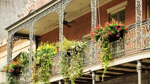 Un balcone con ringhiere in metallo decorate, piante in vaso ed edera pendente.