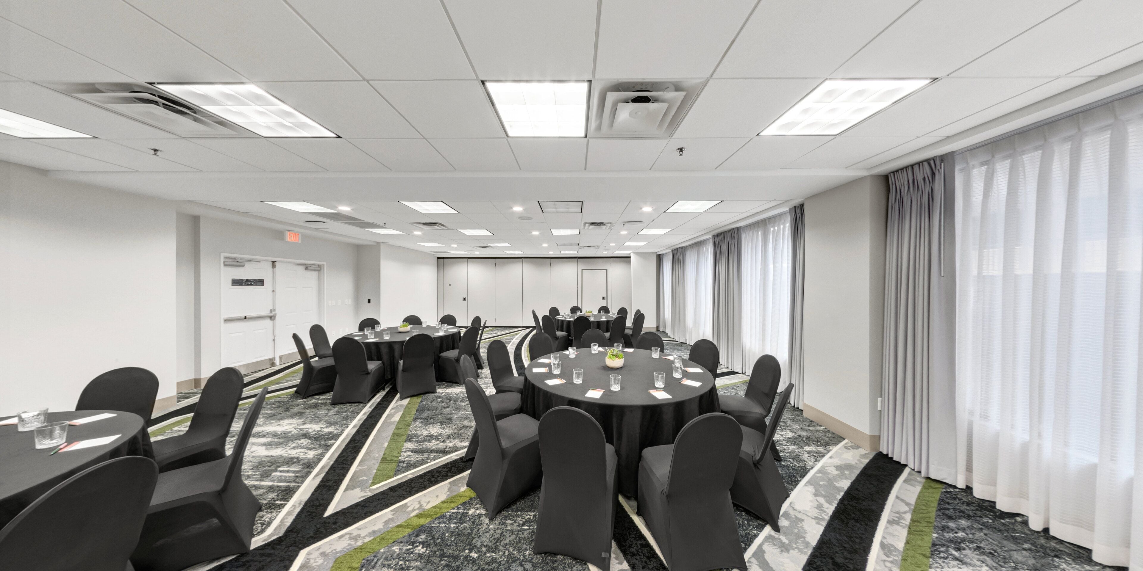 A conference room with round tables, black chairs, and a carpeted floor.