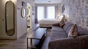 A modern bedroom with a large bed, a sofa, a mirror, and a bedside table.