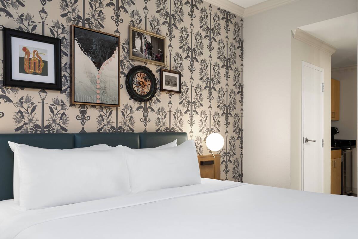 Una cama bien hecha con sábanas blancas, un cabecero verde oscuro y una pared decorada con obras de arte enmarcadas y un papel tapiz estampado.