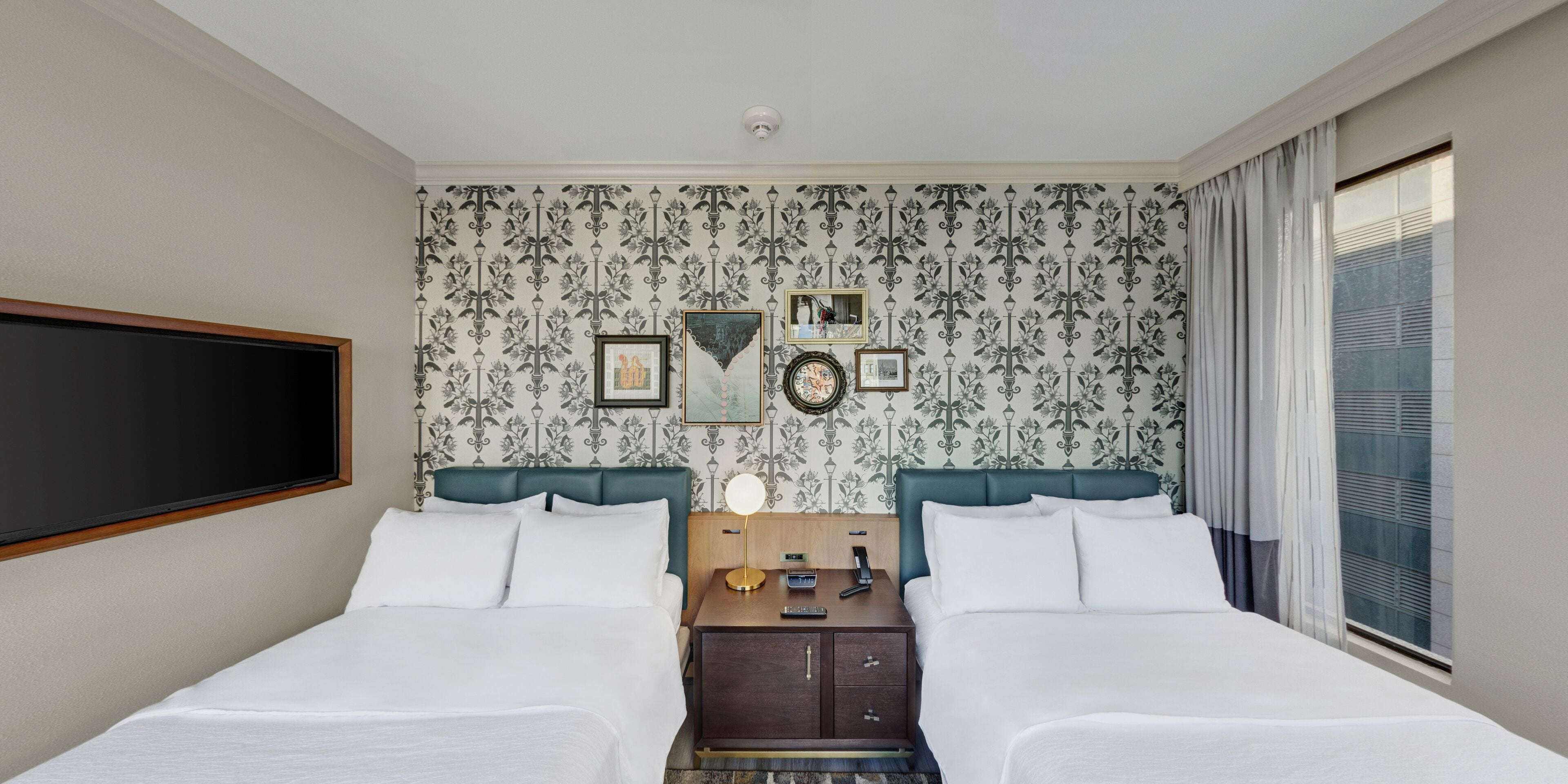 Een hotelkamer met twee bedden, een grote spiegel en een wand met behang met een patroon.