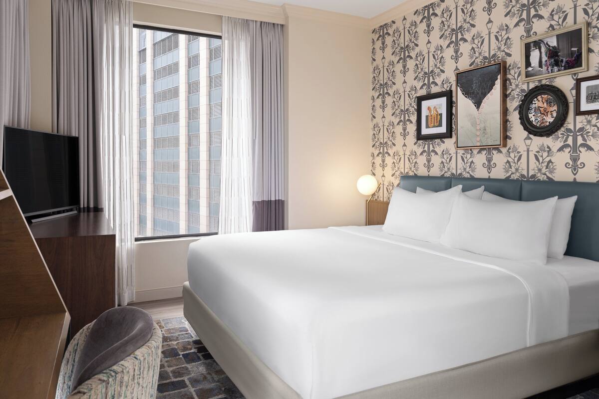 Habitación de hotel con una cama grande, televisión de pantalla plana, escritorio y ventana con cortinas.