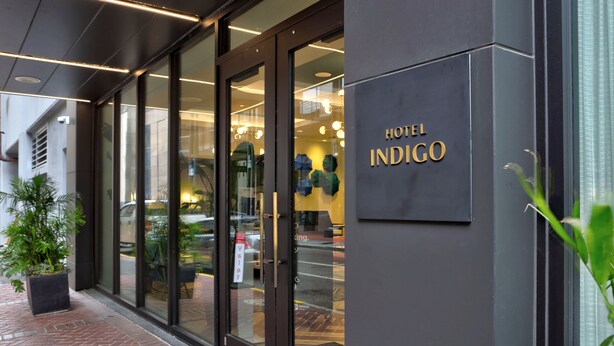 Esterno dell'Hotel Indigo, con un design moderno, ampie finestre in vetro e un cartello con il nome dell'hotel.