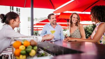 A group of people seated at an outdoor bar with red umbrellas.