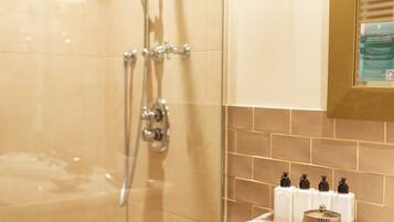 Ein modernes Badezimmer mit Dusche, Waschtisch mit Spiegel und Pflegeprodukten auf der Ablagefläche.