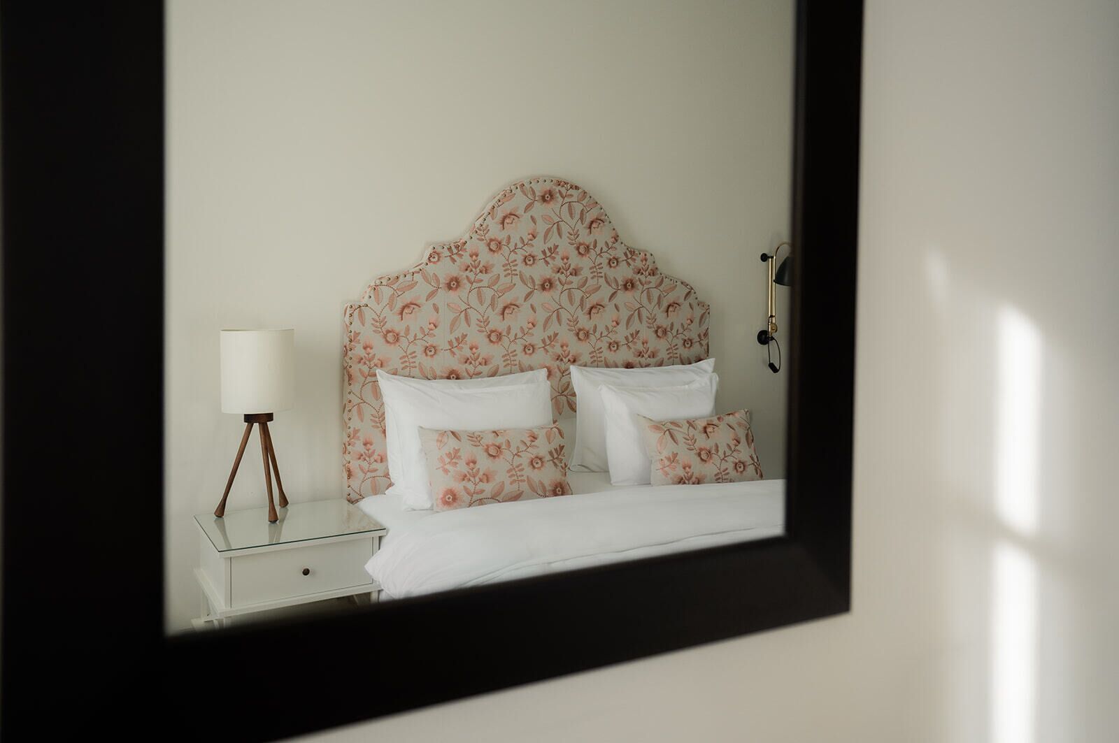 A neatly made bed with floral-patterned headboard and pillows, a bedside lamp, and a small bedside table.