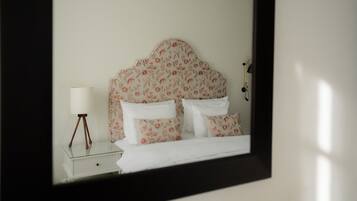 A neatly made bed with floral-patterned headboard and pillows, a bedside lamp, and a small bedside table.