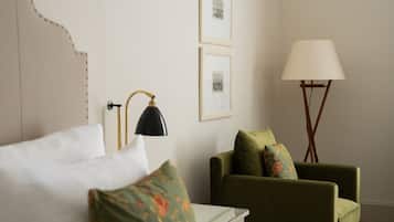 A hotel room with a bed, a green armchair, a floor lamp, and framed pictures on the wall.