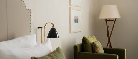 A hotel room with a bed, a green armchair, a floor lamp, and framed pictures on the wall.
