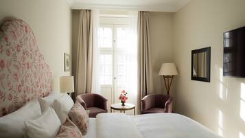 Ein Hotelzimmer mit einem großen Bett, zwei Sesseln, einem kleinen Tisch mit Blumenvase, einer Lampe und einem Fernseher an der Wand.