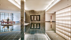Un vestíbulo moderno con piso reflectante, un área de estar con mesa y sillas, y una pared con una serie de luces.