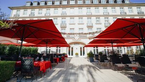 Un patio de hotel con sombrillas rojas, mobiliario exterior y un edificio grande al fondo.
