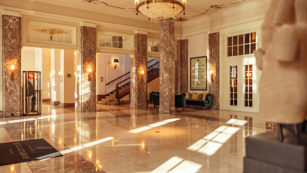 Un vestíbulo espacioso con columnas de mármol, una imponente escalera y una zona de recepción.