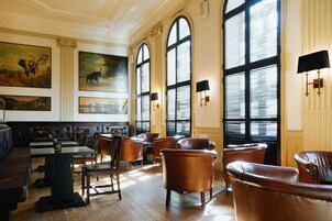 A spacious room with leather armchairs, a wooden floor, and large windows with blinds.