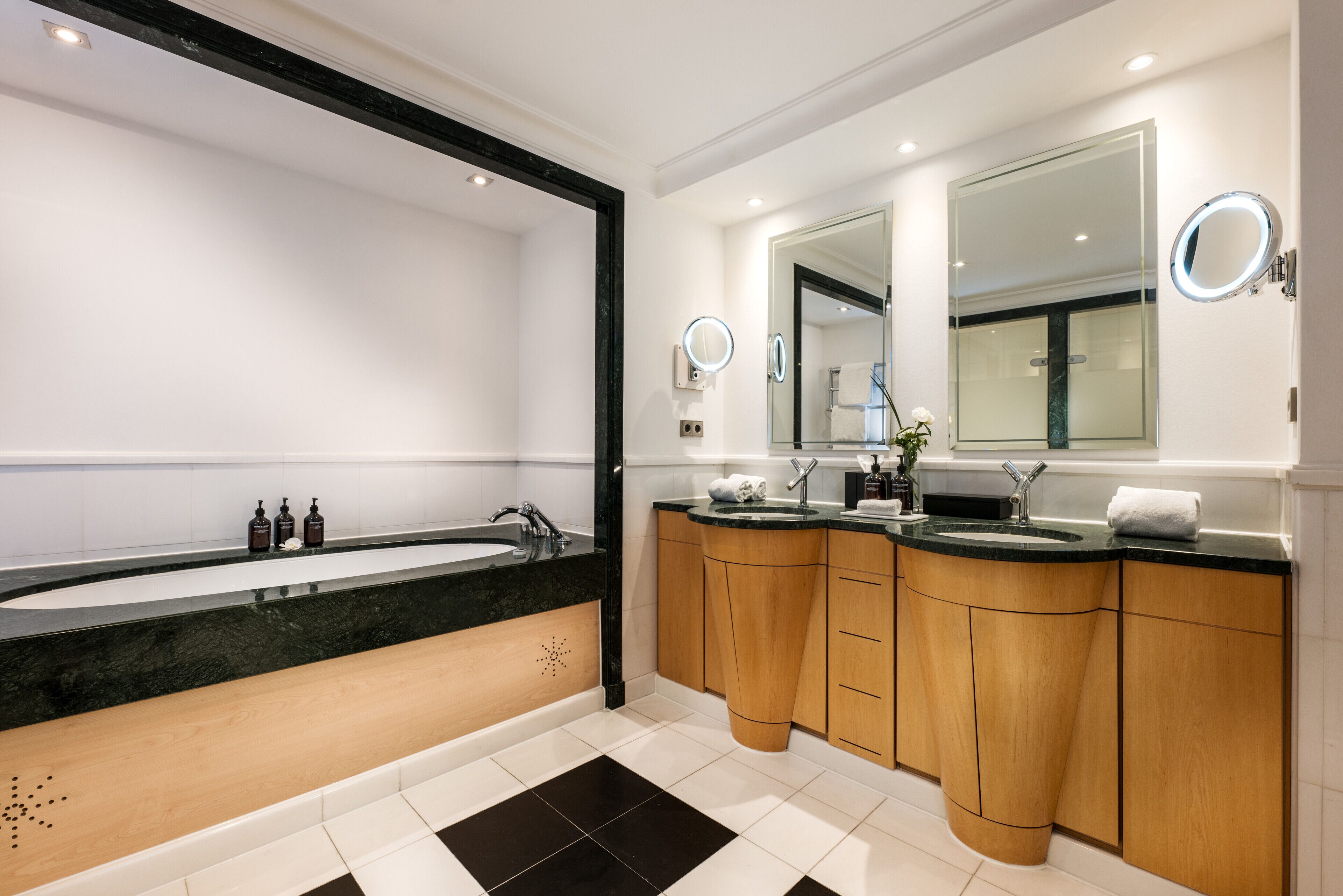 A modern bathroom with a large bathtub, two sinks, wooden cabinets, and a large mirror.