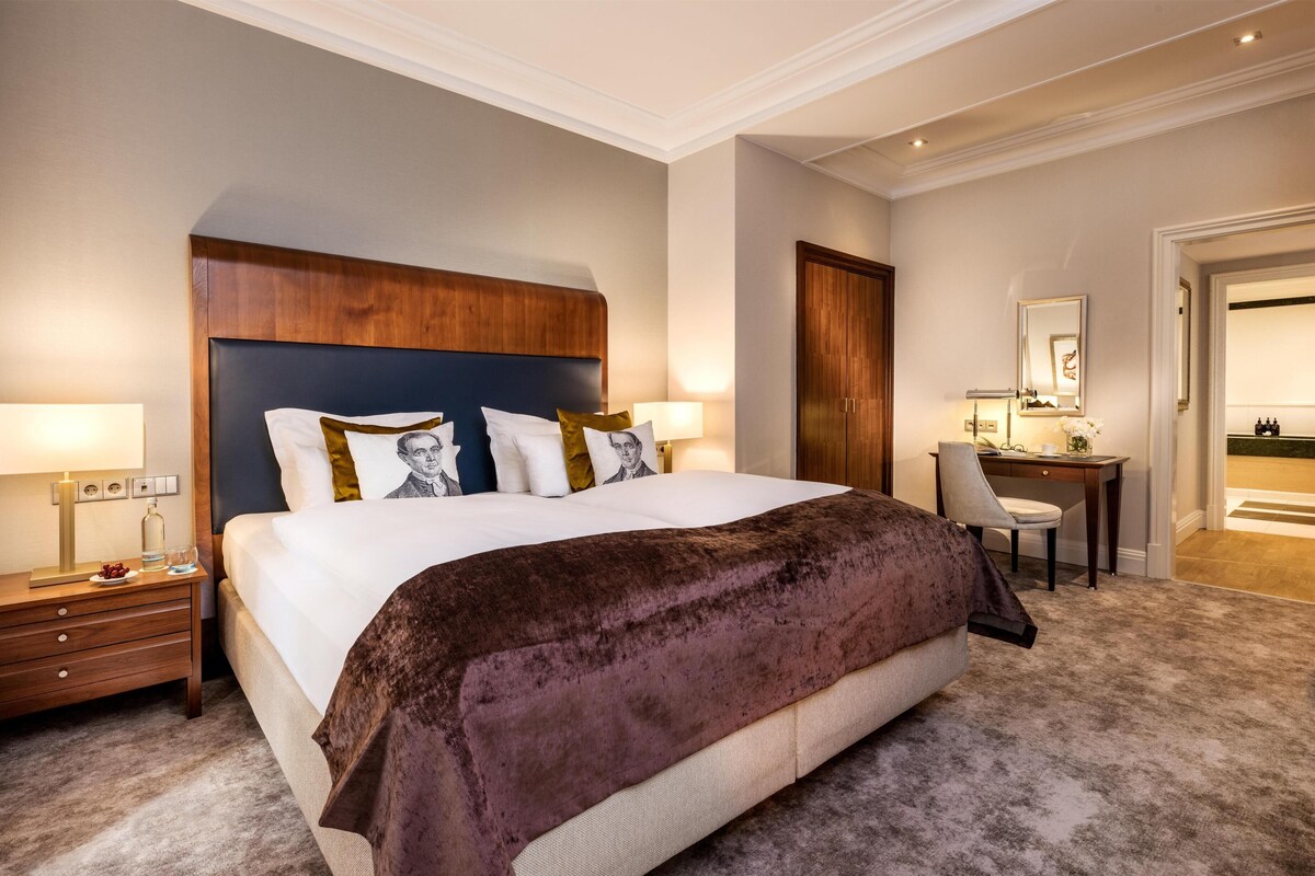 A hotel room with a large bed, bedside tables, a desk, and a mirror.