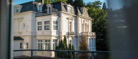 A multi-story building with classical architecture, featuring a balcony and a garden.