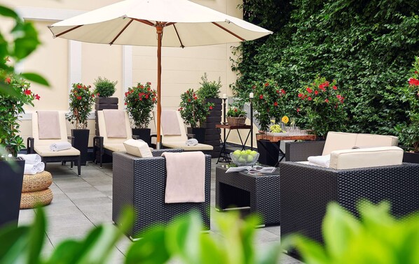An outdoor seating area with wicker furniture, a large umbrella, and potted plants.
