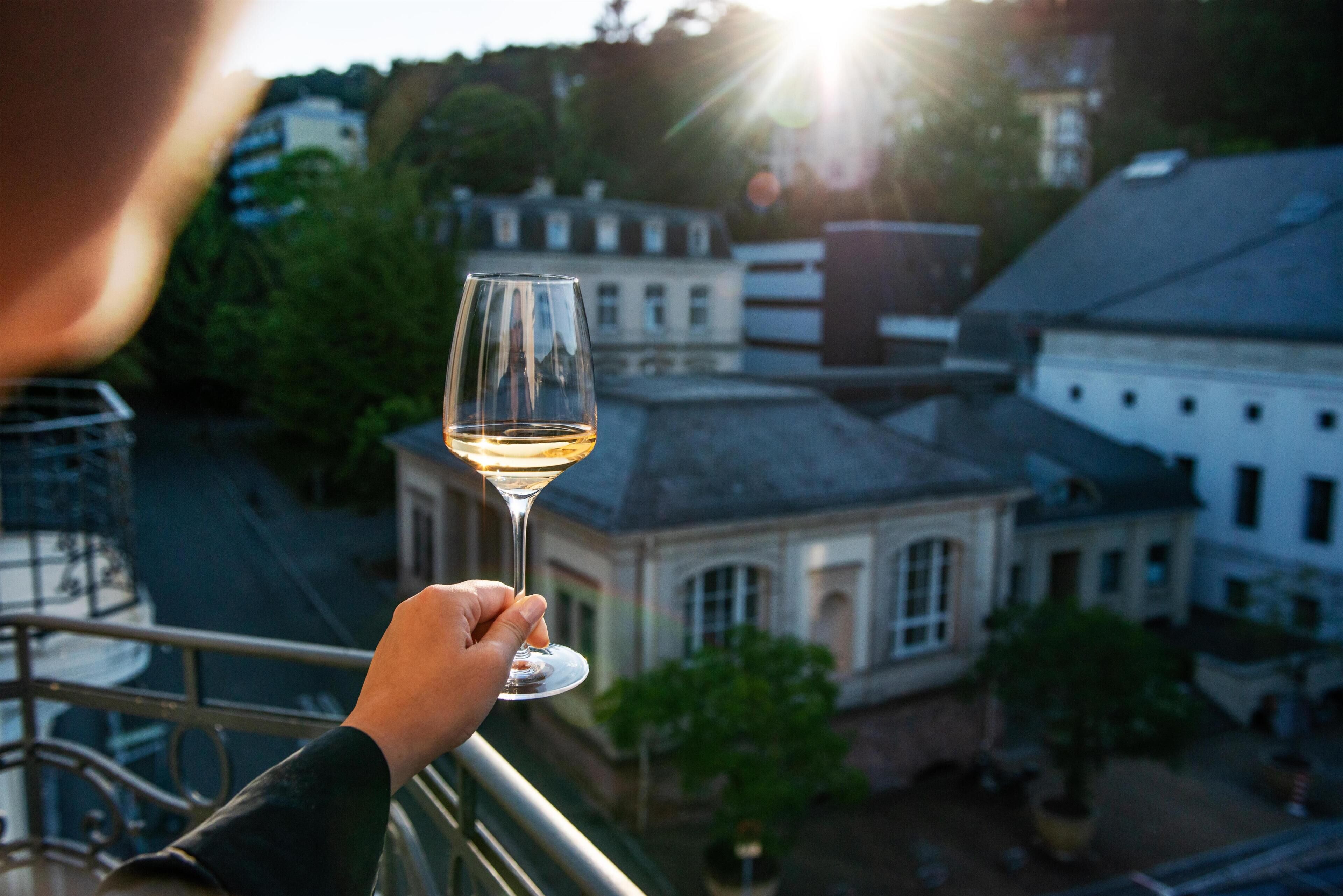 A person holding a wine glass with a view of buildings and trees in the background.