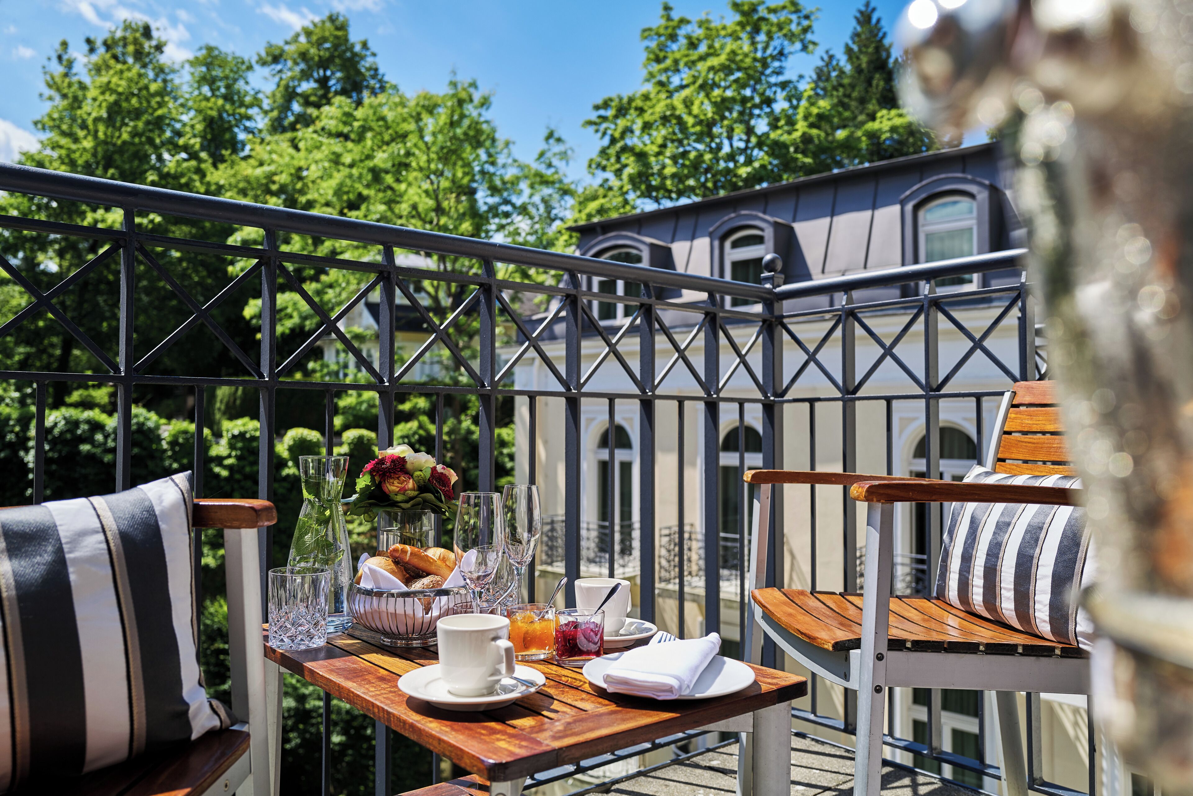 Un balcon avec une table dressée pour le repas, des chaises et une vue sur un immeuble et des arbres.