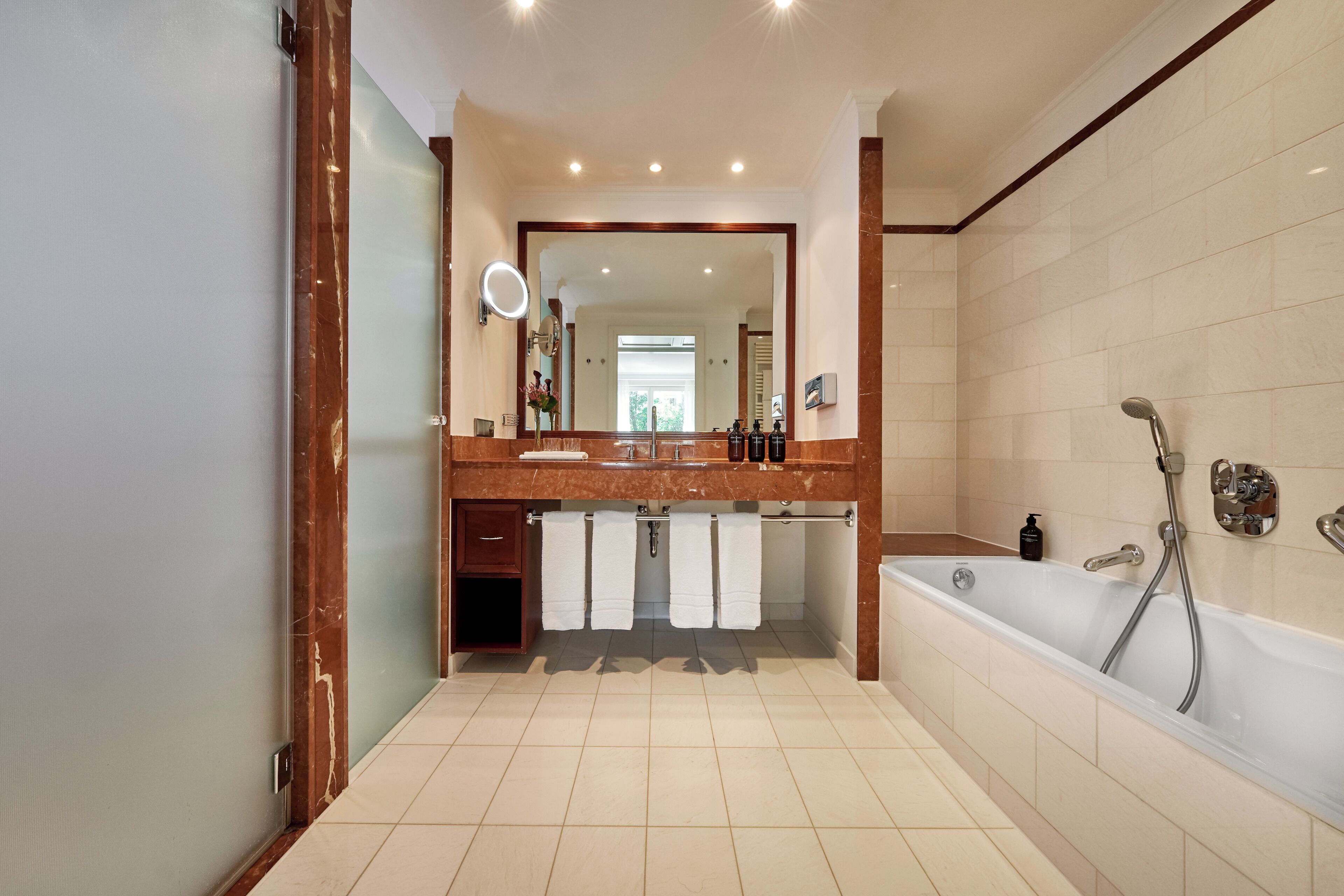 A bathroom with a large mirror, a bathtub, and a vanity with a sink.