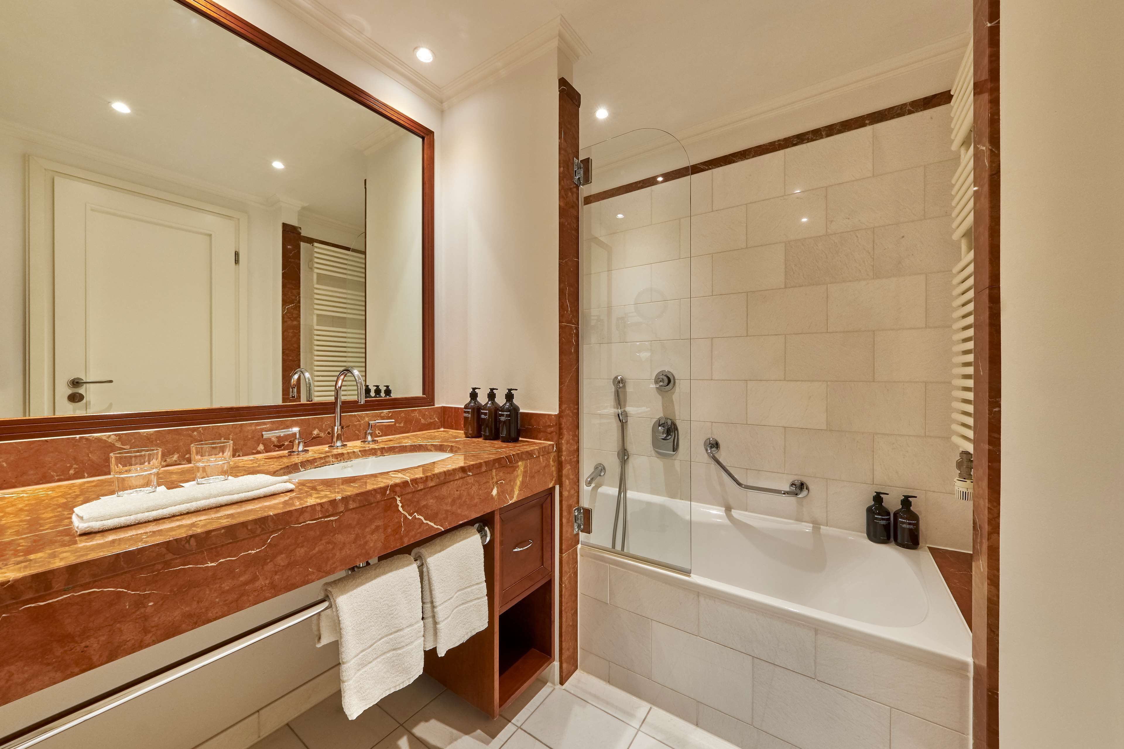 Un baño moderno con tocador de mármol, lavamanos dobles, un espejo grande y zona de ducha separada.
