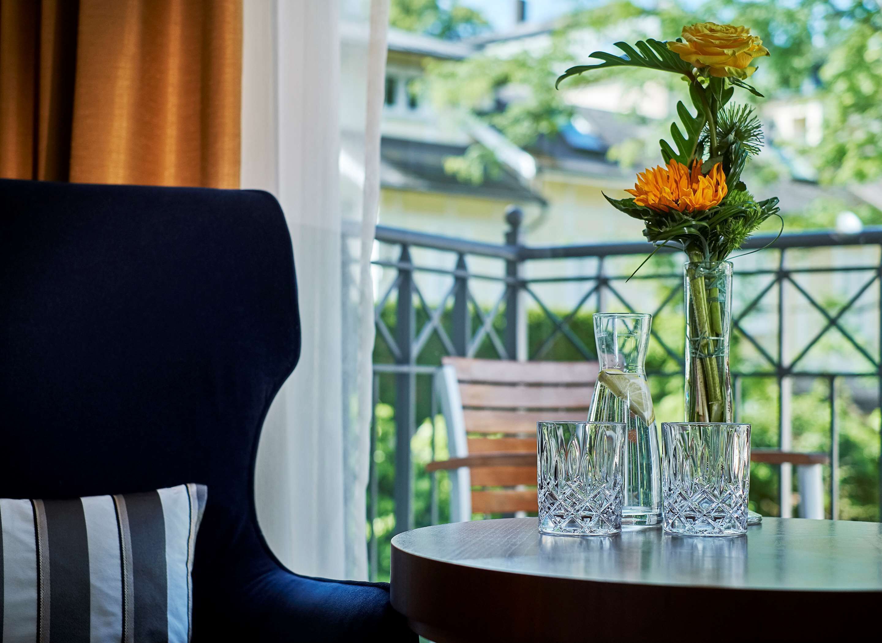 Una mesa con un jarrón de flores y dos vasos en un balcón con vistas a una barandilla y follaje.