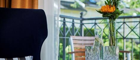 A table with a vase of flowers and two glasses on a balcony overlooking a railing and greenery.