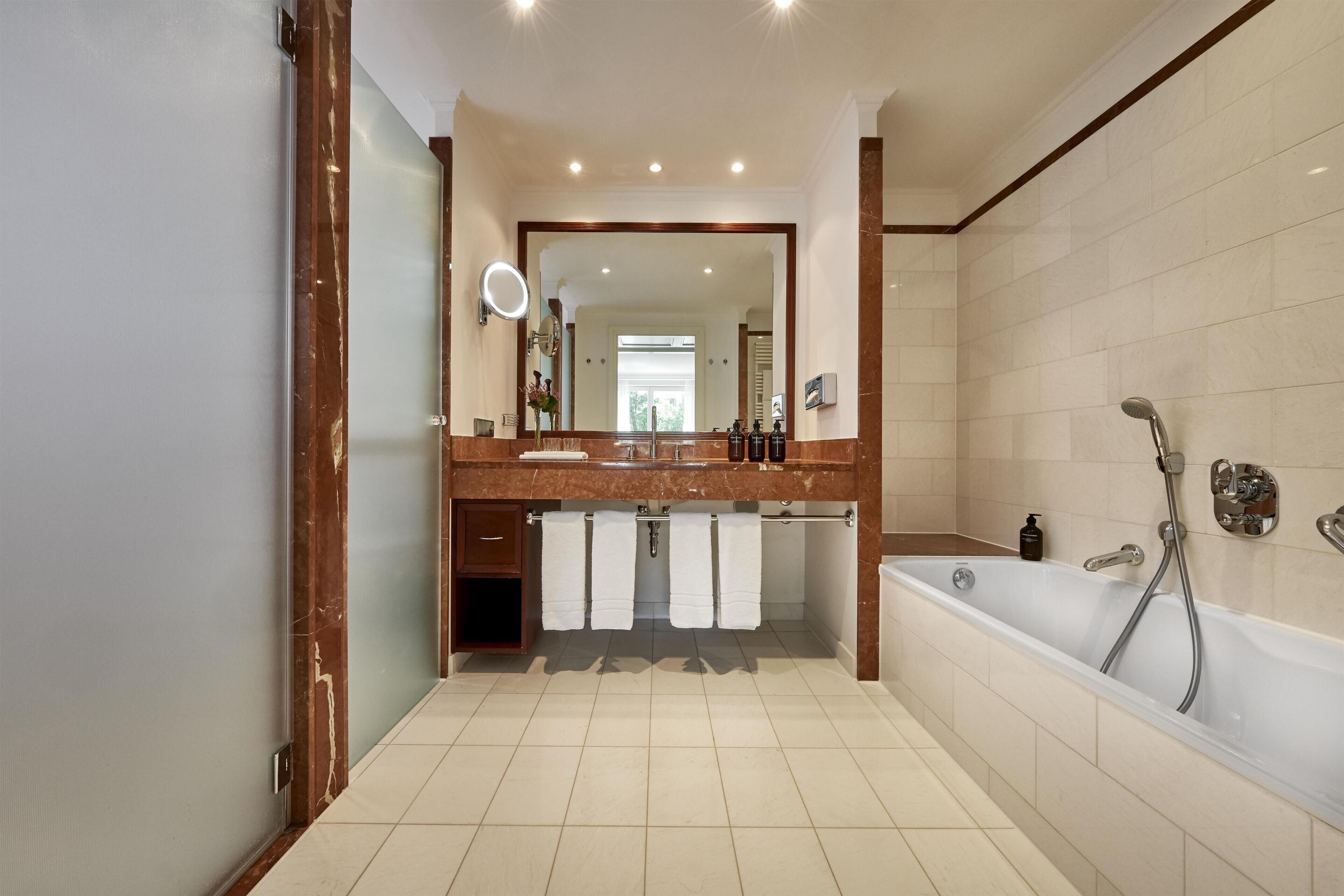 A modern bathroom with a large mirror, a bathtub, and a vanity with a sink.