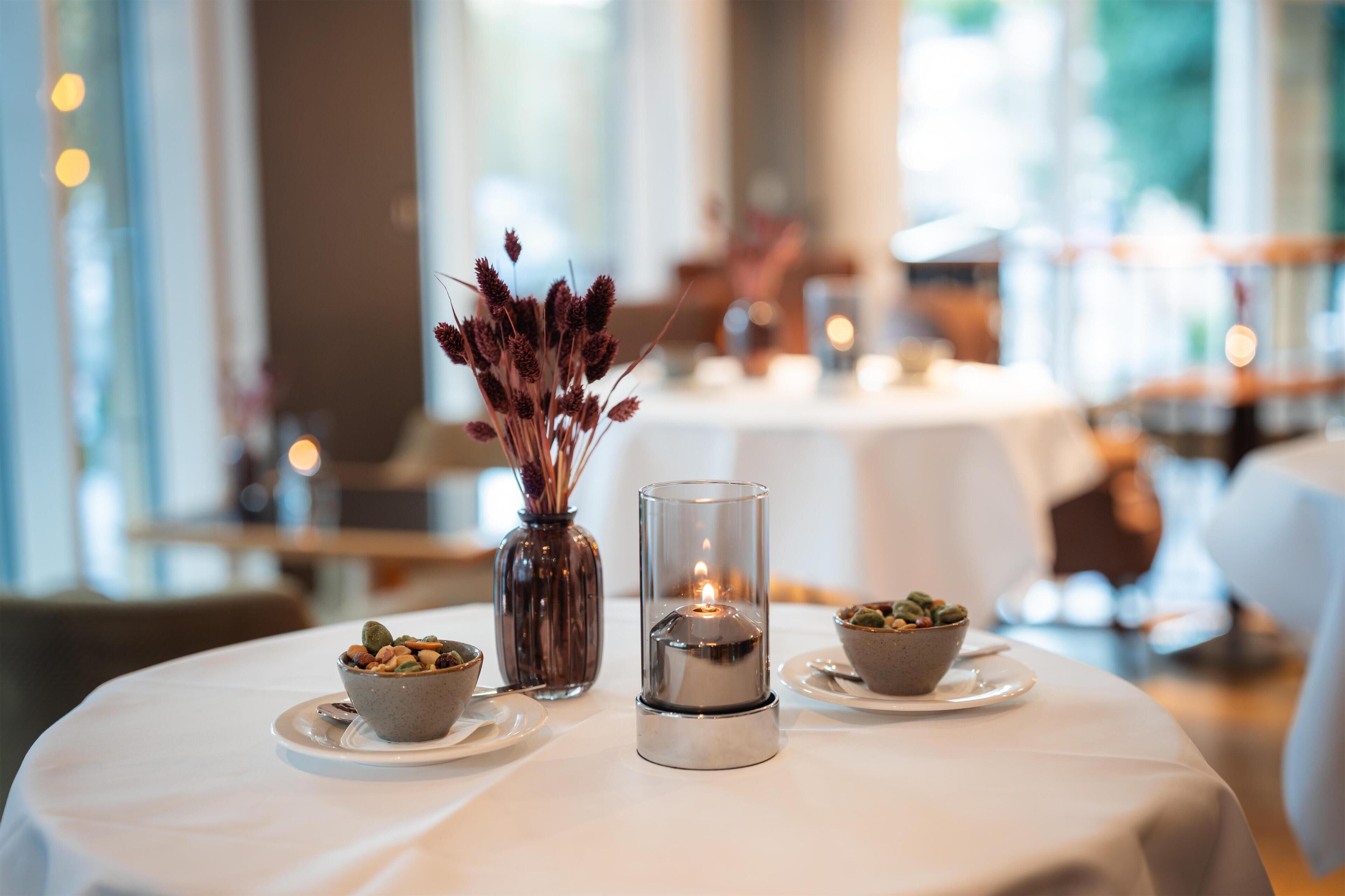 Une table dressée avec une bougie, un vase contenant des plantes séchées et deux petits bols remplis de noix.