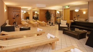 Zona de spa con tumbonas de madera, una mesa de masaje, equipo de ejercicio y un espejo grande.