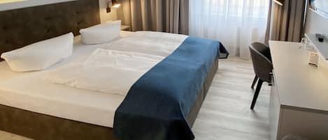Una cama bien hecha con ropa de cama blanca y azul, una lámpara de noche y un escritorio con una silla.