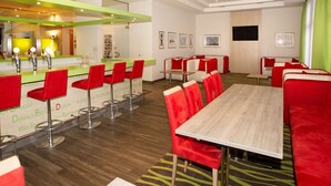 Un moderno vestíbulo de hotel con zona de bar, espacios de estar y una amplia mesa de conferencias.