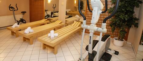 Een sportschool met trainingsapparatuur, houten banken en potplanten.