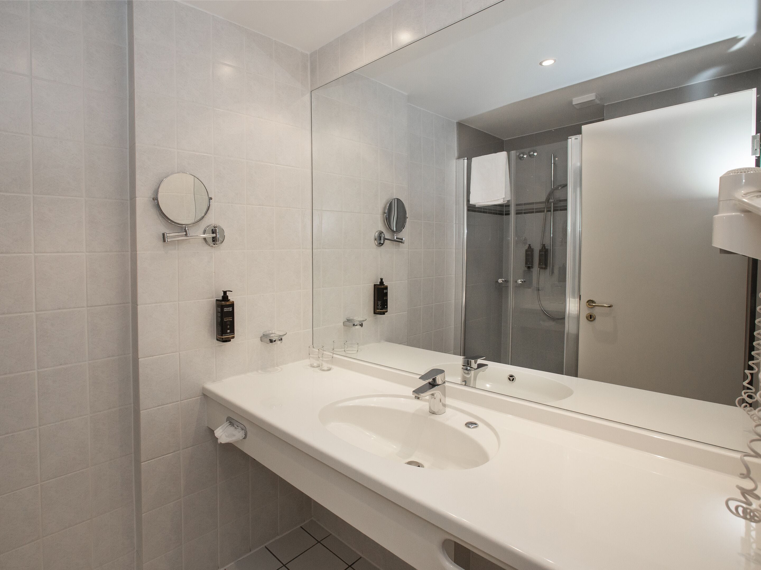 A modern bathroom with a large mirror, a white sink, and a glass shower enclosure.
