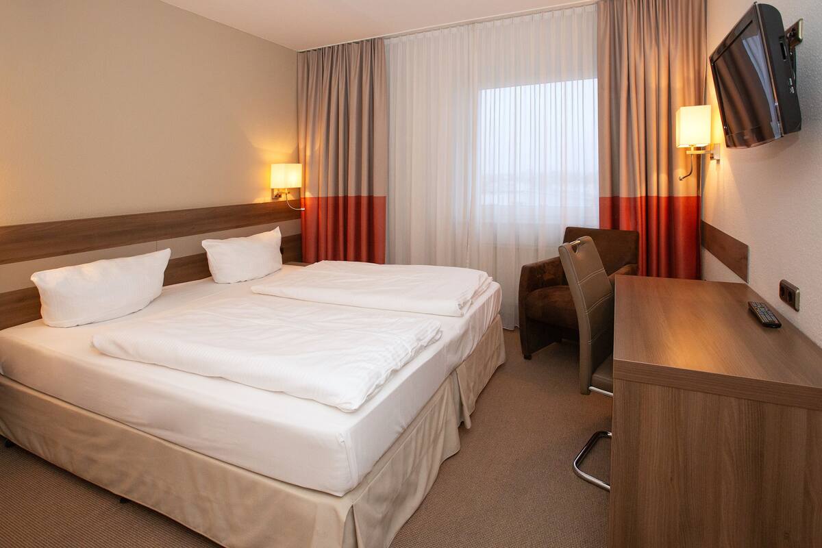 Una habitación de hotel con dos camas, un escritorio, una silla, un televisor y cortinas.