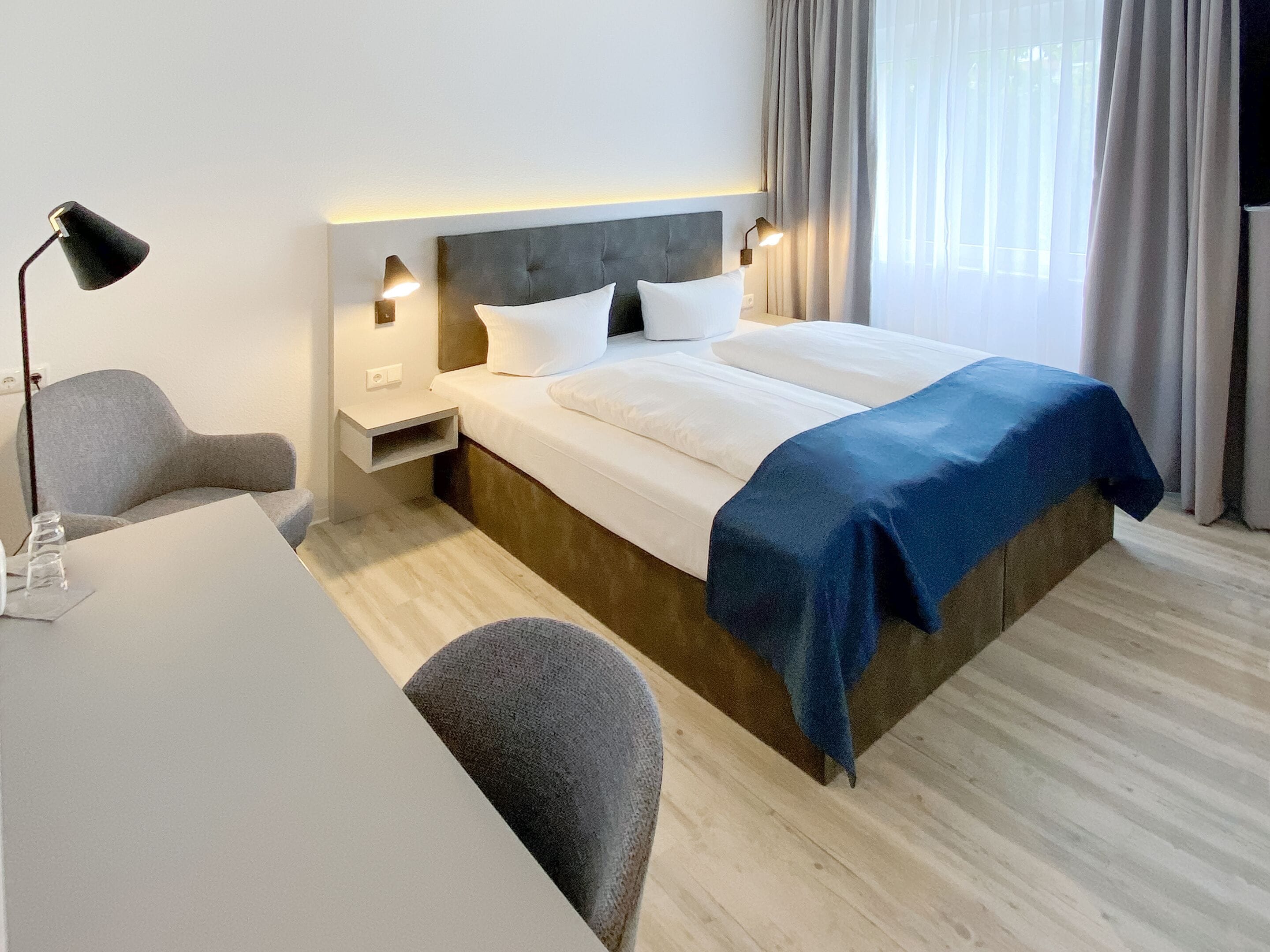 A modern hotel room with a large bed, bedside tables, a desk, and a chair.