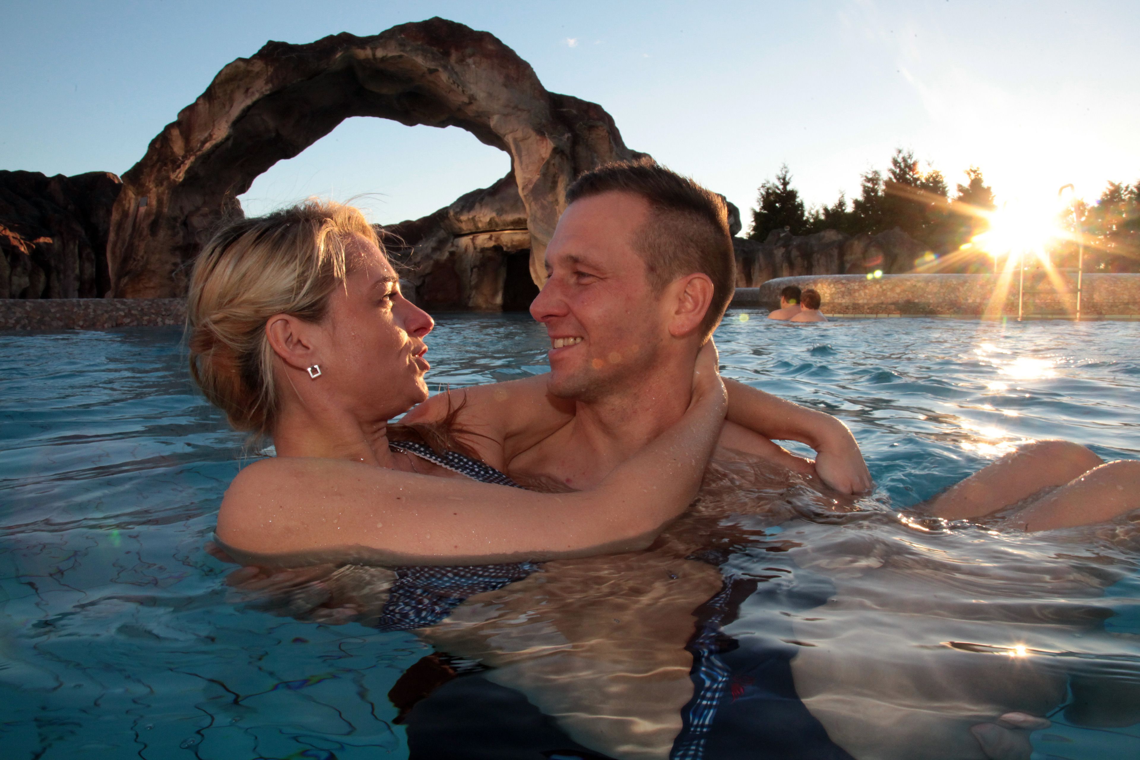 Un couple dans une piscine, avec une formation rocheuse naturelle en arrière-plan.