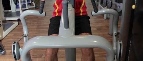 A man exercising on a stationary bike in a gym with various equipment in the background.